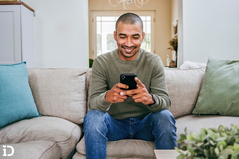 man sitting on a couch and texting on his smartphone