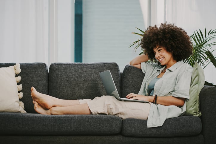 woman smiling and sitting on the couch browsing online