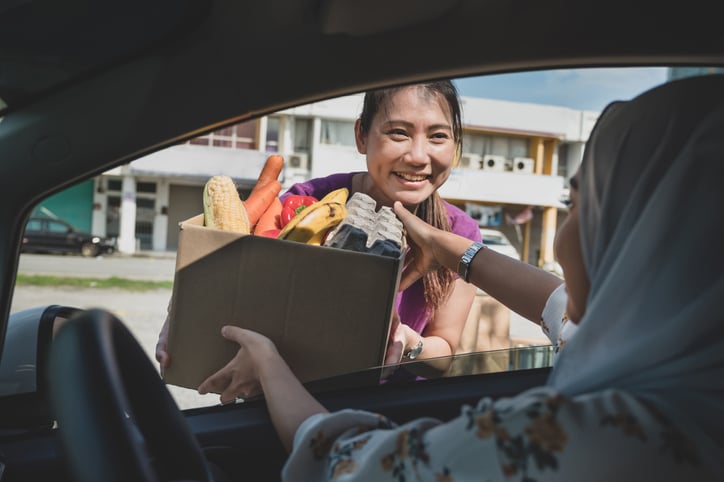 woman handing a box of food to another woman in a car