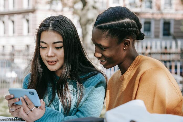 two young women sitting and watching a video on a phone